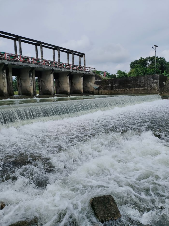 why-choose-us-02 Scenic view of a hydroelectric dam over a river in Sylhet, Bangladesh showcasing flowing water and lush surroundings.
